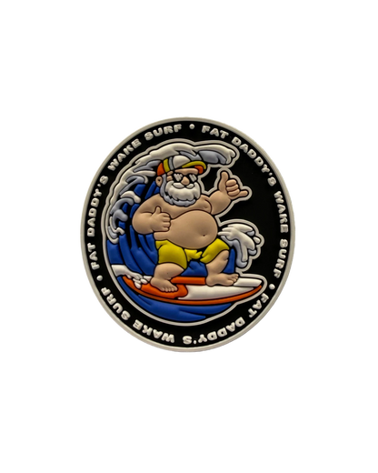 A circular enamel coin or medallion featuring a cartoon surfer character on a white surfboard against a black background, with the text 'FAT DADDY'S WAVE SURF' around the edge.
