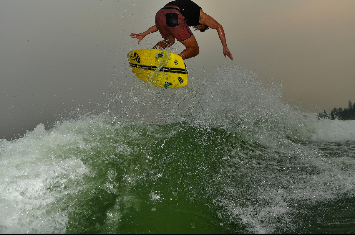 Man wakeboarding above a green wave with yellow board