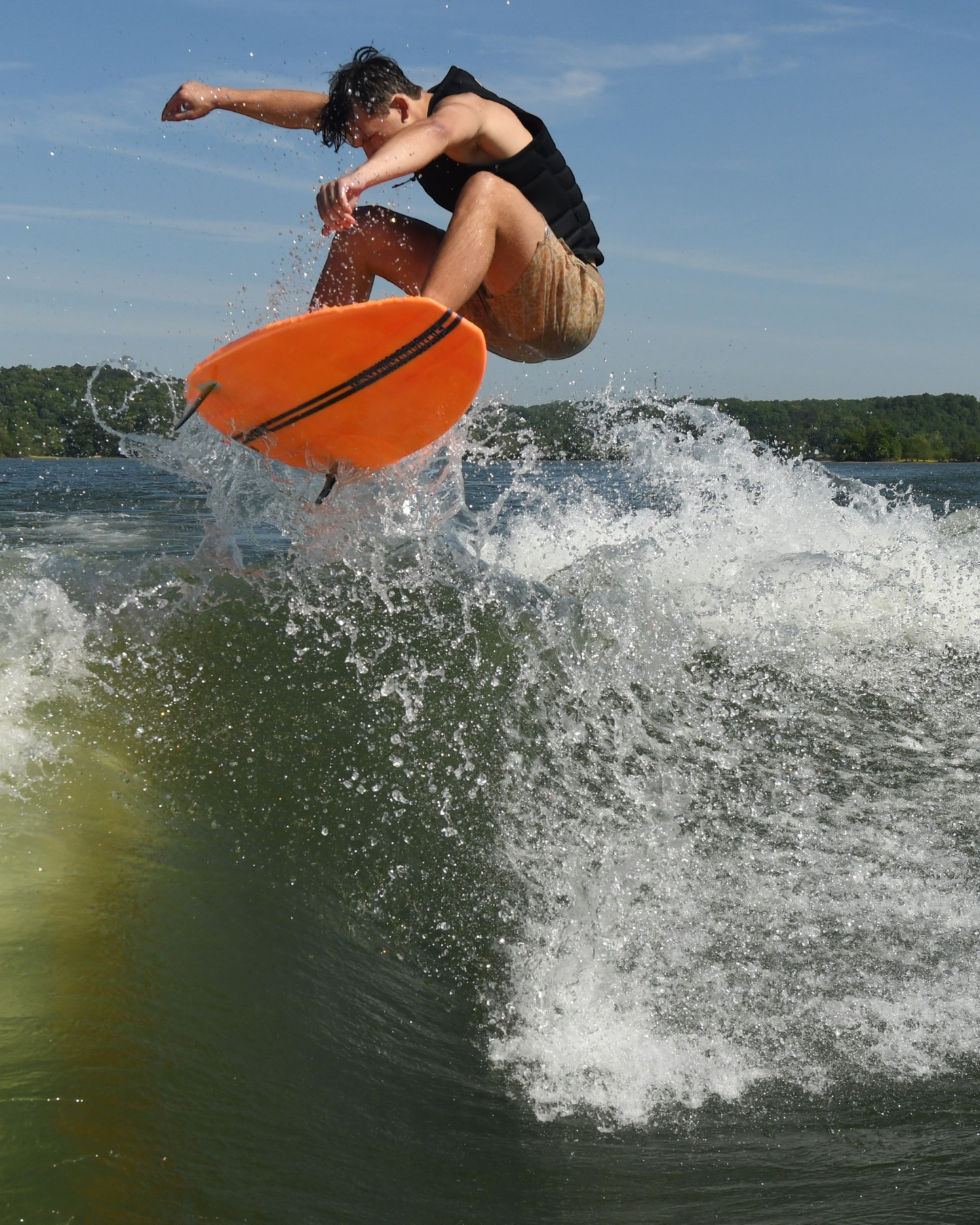 Fat Daddy's Wake Surf Barrette Greenroom wakesurf board in bright orange performing an aerial trick on a lake wave
