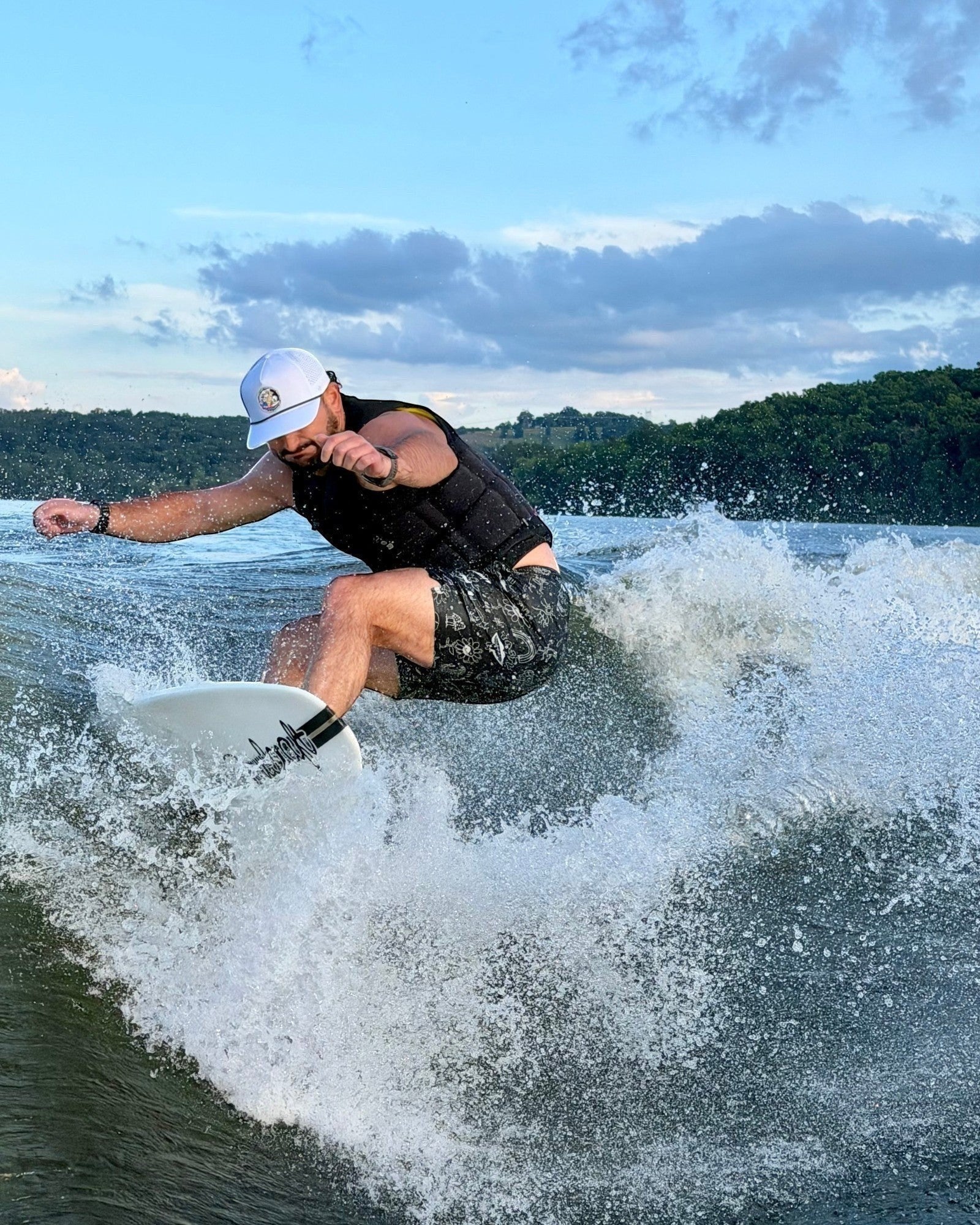 Man wearing a white Fat Daddy's Wake Surf waterproof rope hat while wakesurfing on a lake
